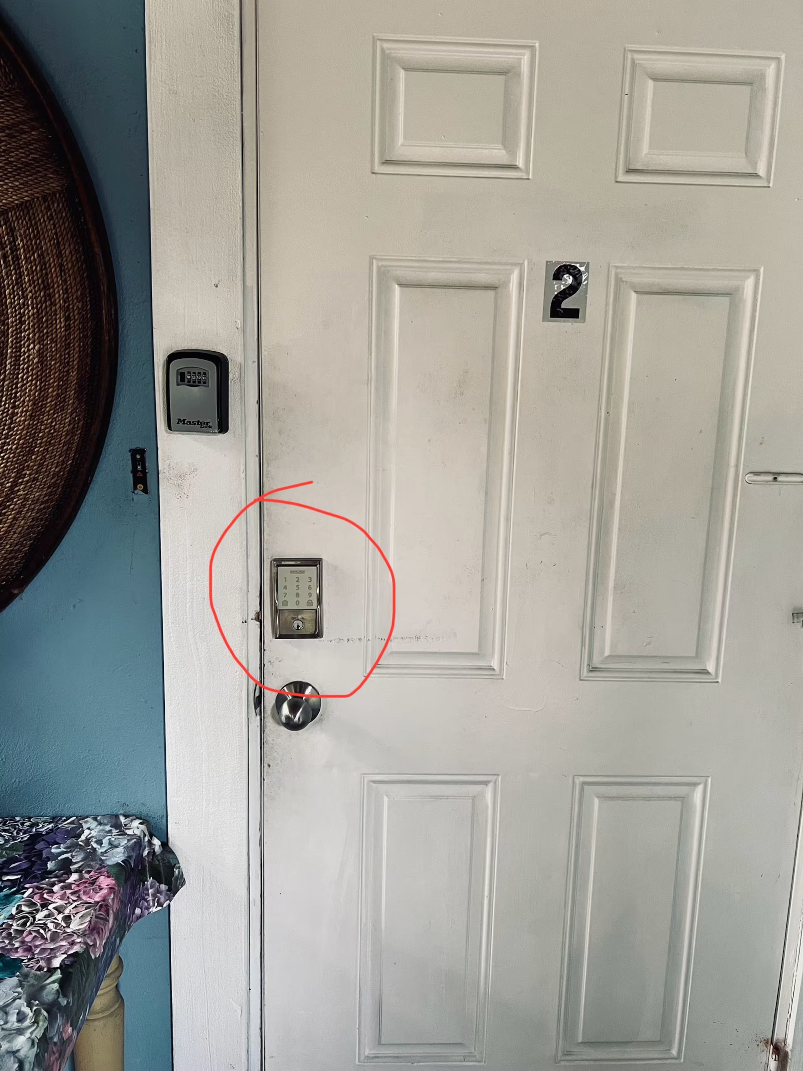 A white door with a numeric keypad lock, a small electronic device above it, and a red circle highlighting a specific area.