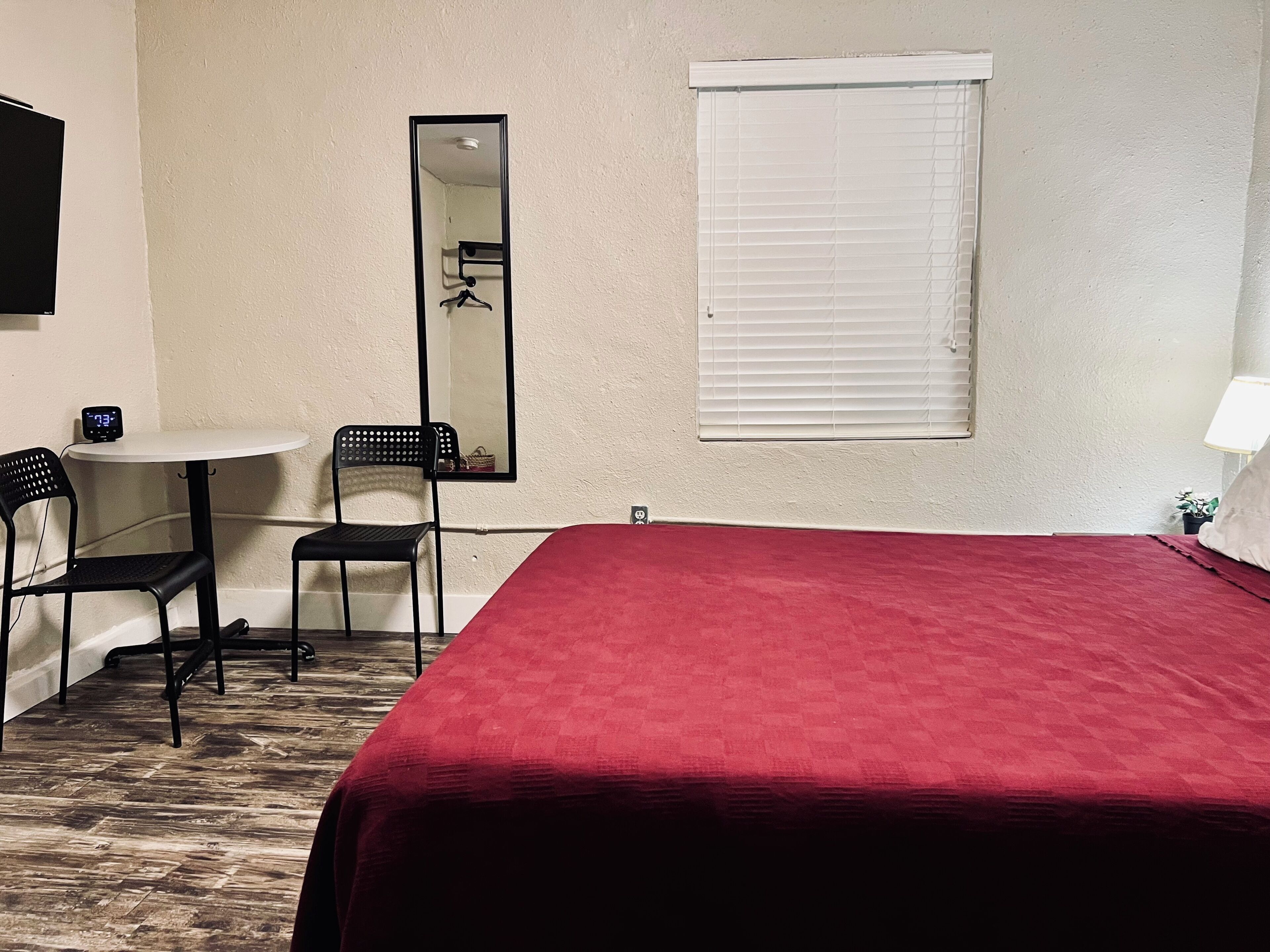 A hotel room with a bed, a small round table, two chairs, a mirror, and a window with blinds.
