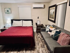 A bedroom with a bed, a sofa, an air conditioner, a framed picture, and a lamp. - Unit 2 - Private Queen Studio Near Miami Airport & Wynwood (Miami)