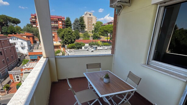 A balcony with a table and chairs, a potted plant, and a view of buildings and trees. - Raffaele's apartment, Tranquility and comfort, Suitable for small groups and families (Roma)