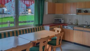 A kitchen with a dining area, a microwave, a sink, and a window with a view of a house and lawn. - Holiday Home 'Landlhof' with Mountain View, Private Terrace and Wi-Fi (Ramsau)