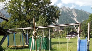 A playground with swings, a slide, and a green shed. - Holiday Home 'Landlhof' with Mountain View, Private Terrace and Wi-Fi (Ramsau)