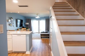 A modern kitchen with a central island, a dining area with a sofa, and a staircase leading to another level. - Renovated Beach Condo Balcony, Pool/BBQ | CoqB202 (St. Augustine)