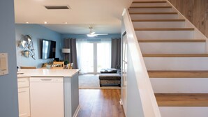 Eine moderne Küche mit Geschirrspüler, ein Essbereich mit Tisch und Stühlen, eine Treppe und ein Wohnbereich mit Sofa und Fernseher.