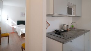 A compact hotel room with a bed, bedside table, and a small kitchenette with a sink and microwave.