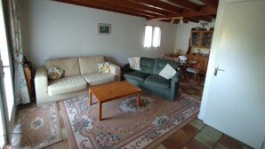 A living room with a beige sofa, a green sofa, a wooden coffee table, and a patterned rug. There is a door to the right and a window with curtains in the background. - House in lovely gardens with shared pool in Dordogne, parking on site (Bouteilles Saint-Sébastien)