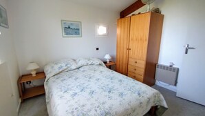 A bedroom with a bed, a wooden wardrobe, a nightstand, a wall-mounted fan, and a radiator. - House in lovely gardens with shared pool in Dordogne, parking on site (Bouteilles Saint-Sébastien)