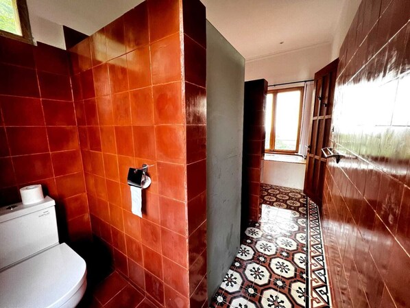 A bathroom with red tiles, a toilet, and a patterned floor.