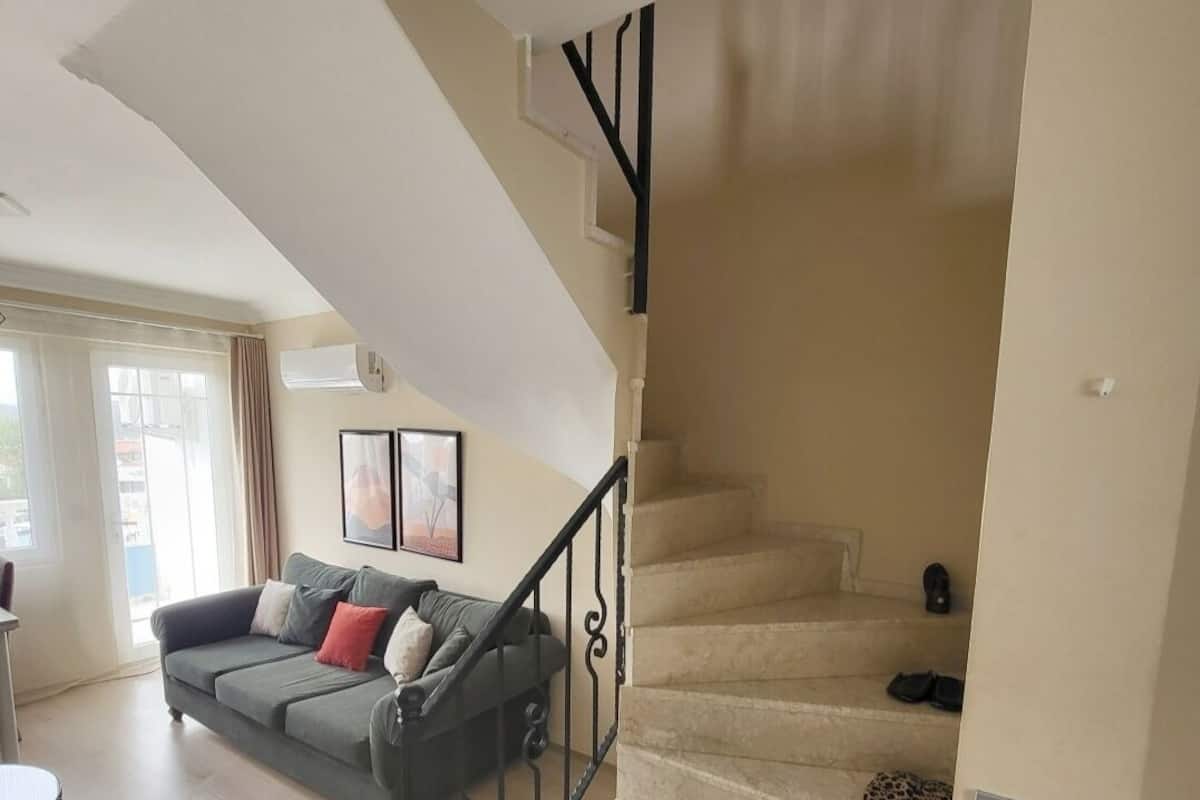 A living room with a sofa, a staircase, and a door leading to another room.