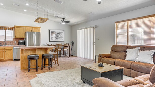 A modern kitchen with wooden cabinets, a stainless steel refrigerator, and a dining area with a bar stool set. - Near Golf Courses: Poolside Paradise in Yuma! (Yuma)
