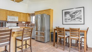 A kitchen with wooden cabinets, a stainless steel refrigerator, a microwave, and a dining area with wooden chairs. - Near Golf Courses: Poolside Paradise in Yuma! (Yuma)