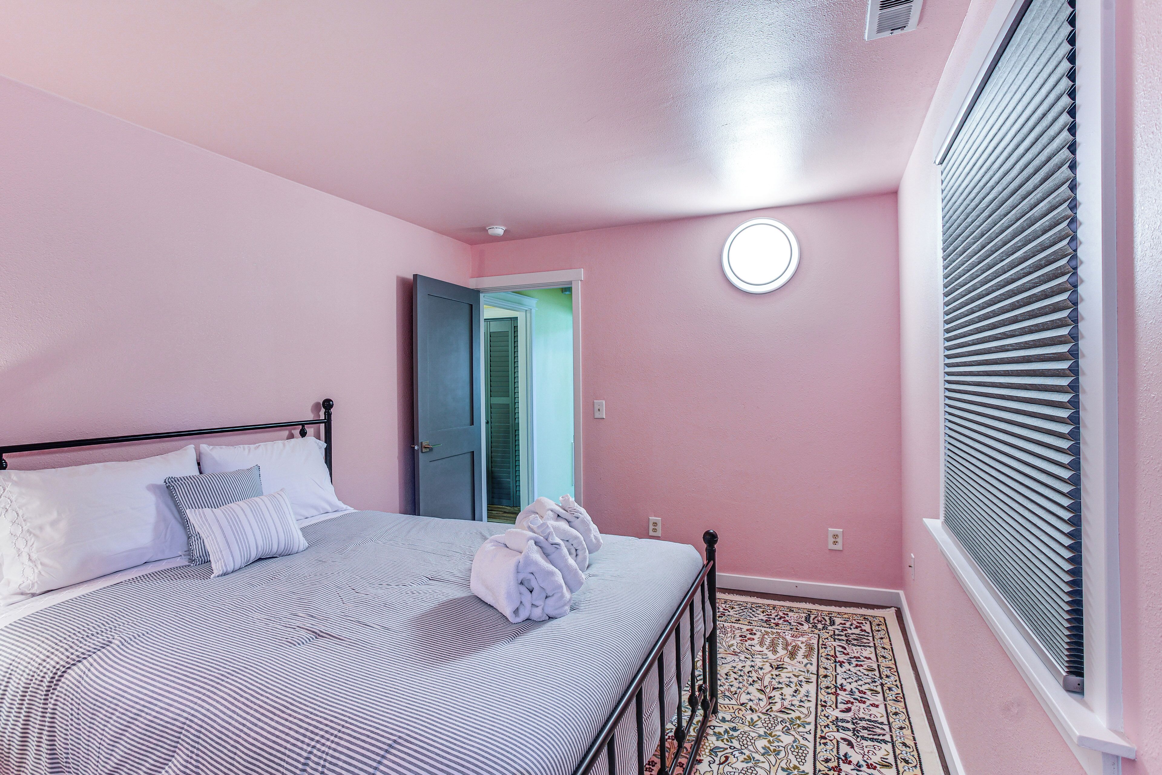 Une chambre à coucher avec un lit, des oreillers, une fenêtre avec des stores, une porte et un tapis à motifs.