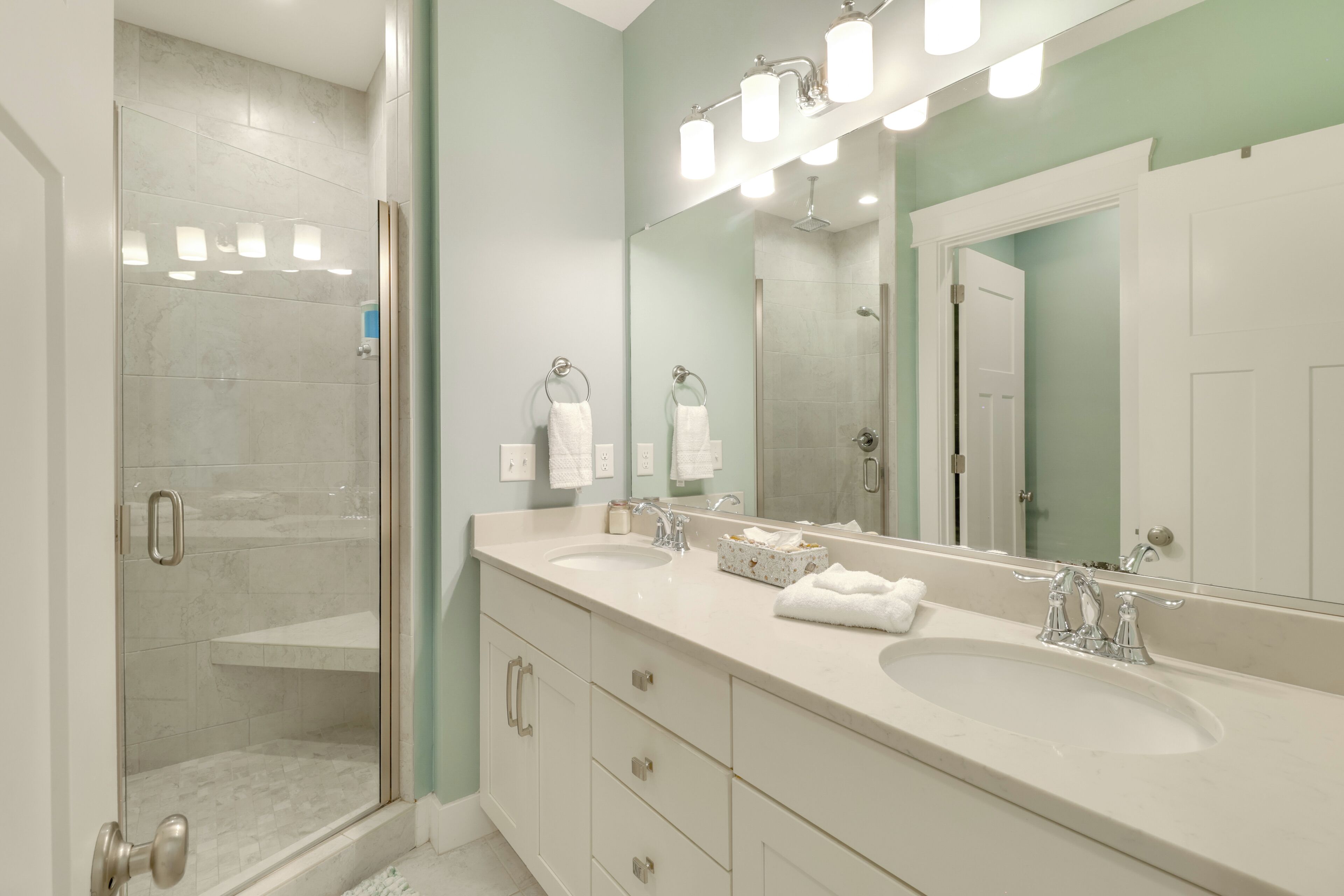 A bathroom with two sinks, a glass shower enclosure, and a large mirror with lights.