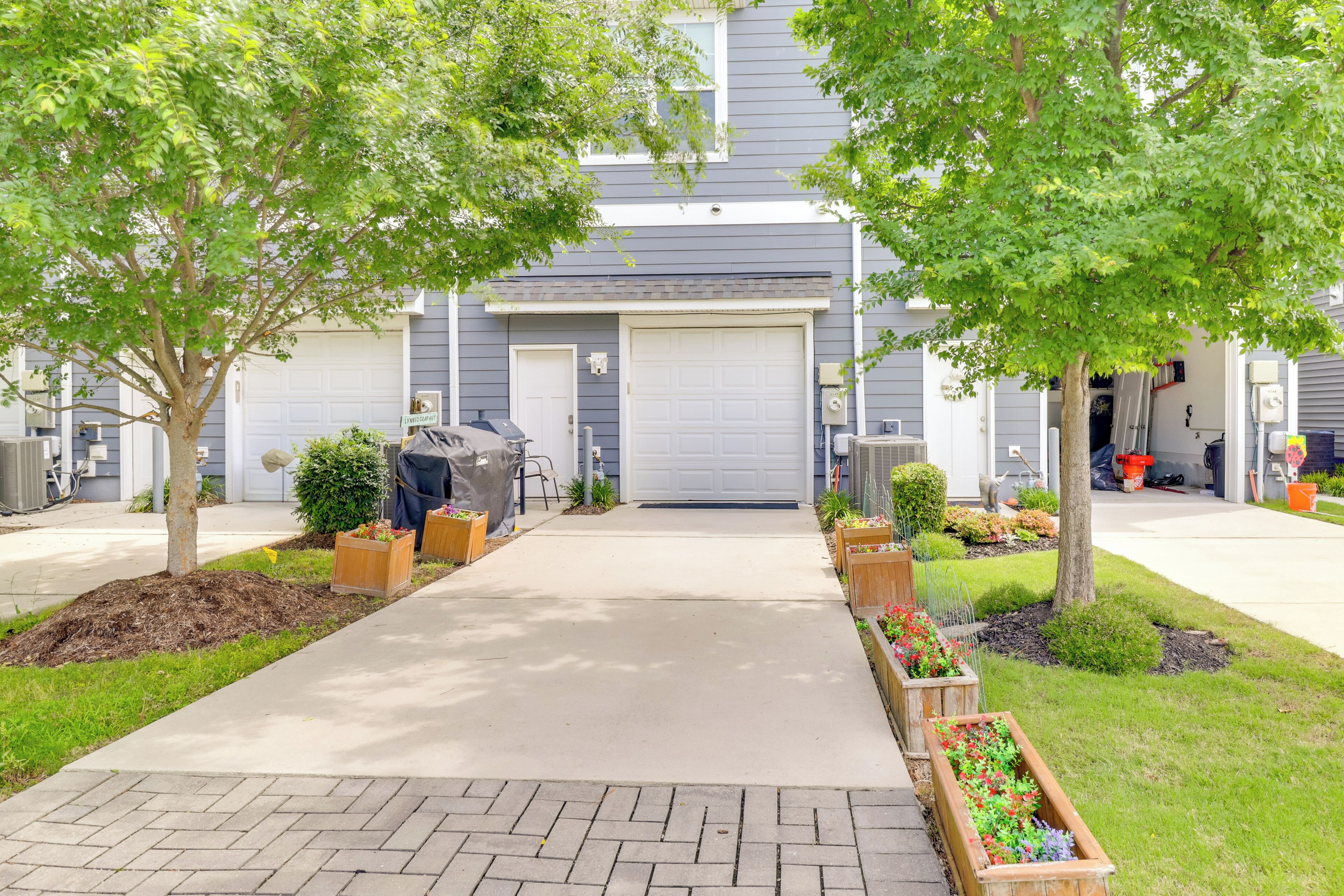 Une allée menant à une maison et aboutissant à un garage, entourée d’espaces aménagés avec des arbres et des parterres de fleurs.
