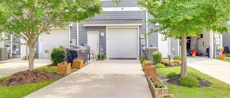 Une allée menant à une maison et aboutissant à un garage, entourée d’espaces aménagés avec des arbres et des parterres de fleurs.