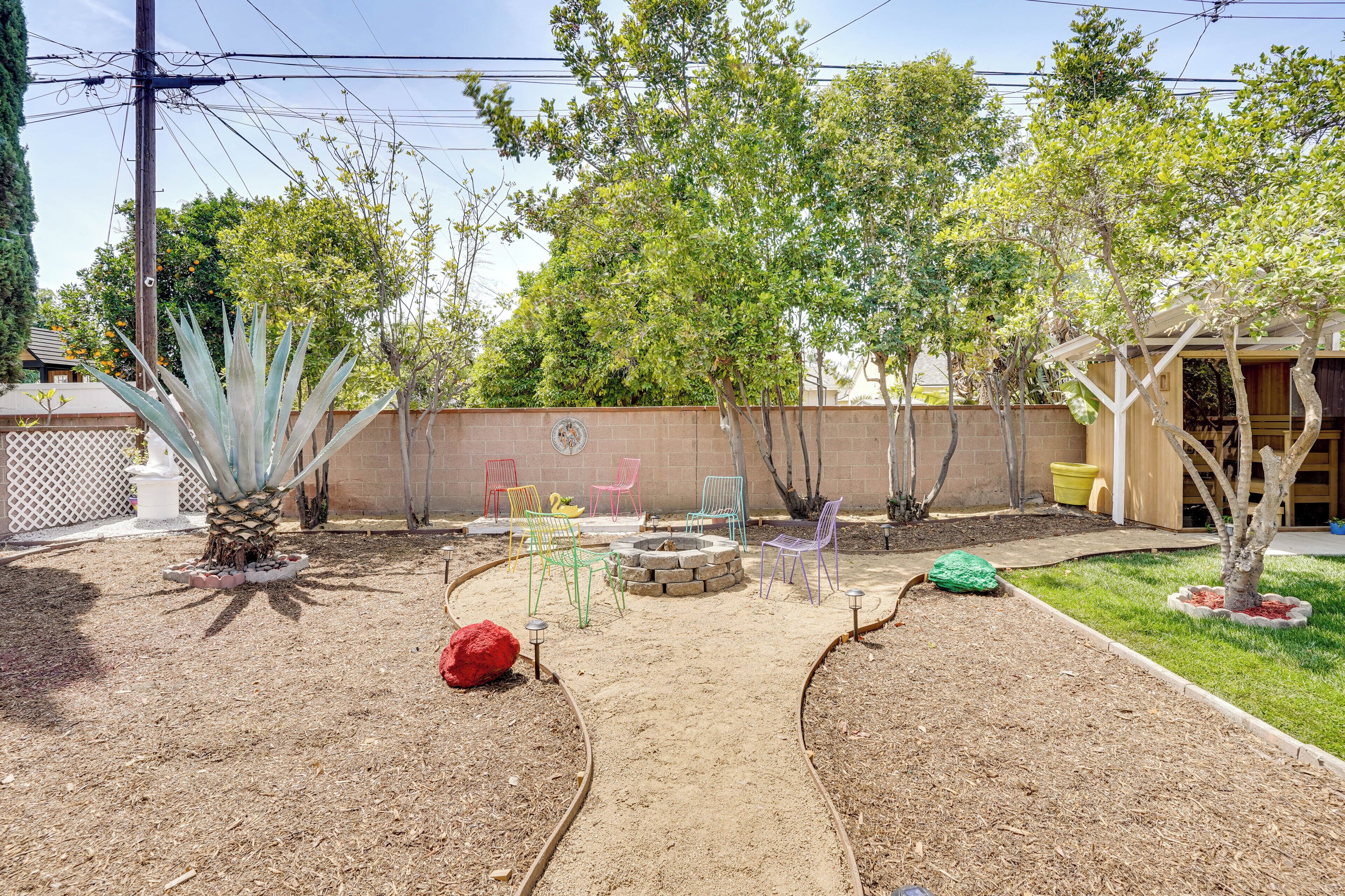 A backyard with a fire pit, colorful chairs, and a small tree.
