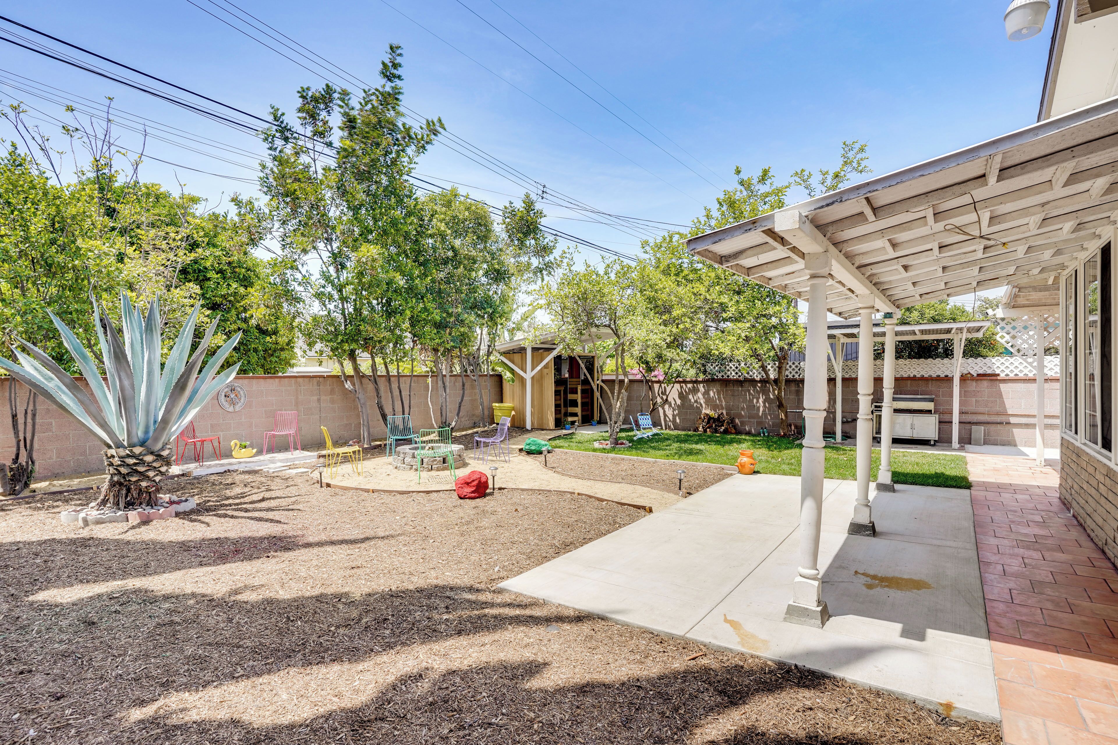 Un jardín trasero con un patio, mobiliario exterior, una palmera y un área techada.