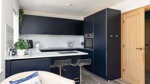 A modern kitchen with dark cabinets, a white countertop, and a wooden door. - Coastal Retreat With Hot Tub Walk to Beach (Chichester)