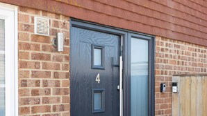A modern door with a number "4" on it, set in a brick wall with a wooden fence nearby. - Coastal Retreat With Hot Tub Walk to Beach (Chichester)