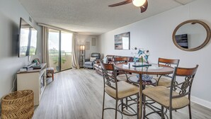 Un vaste espace dédié à la salle à manger, comprenant une table ronde et des chaises, un ventilateur de plafond et une grande fenêtre agrémentée de rideaux.