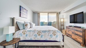 Une chambre d’hôtel avec un lit, une télévision, une commode et un balcon équipé de chaises.