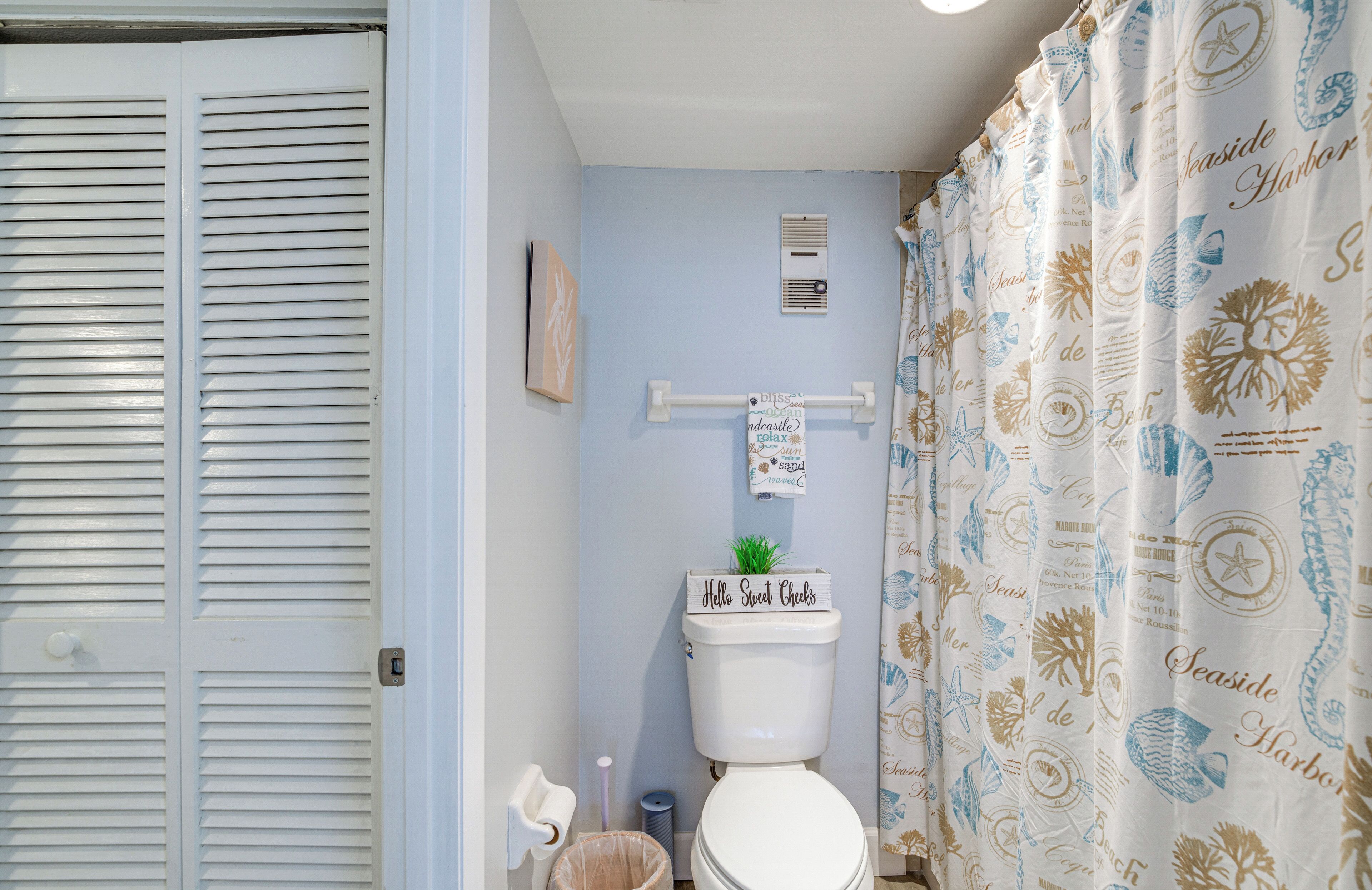 Un baño con inodoro, toallero y cortina de ducha con motivos náuticos.