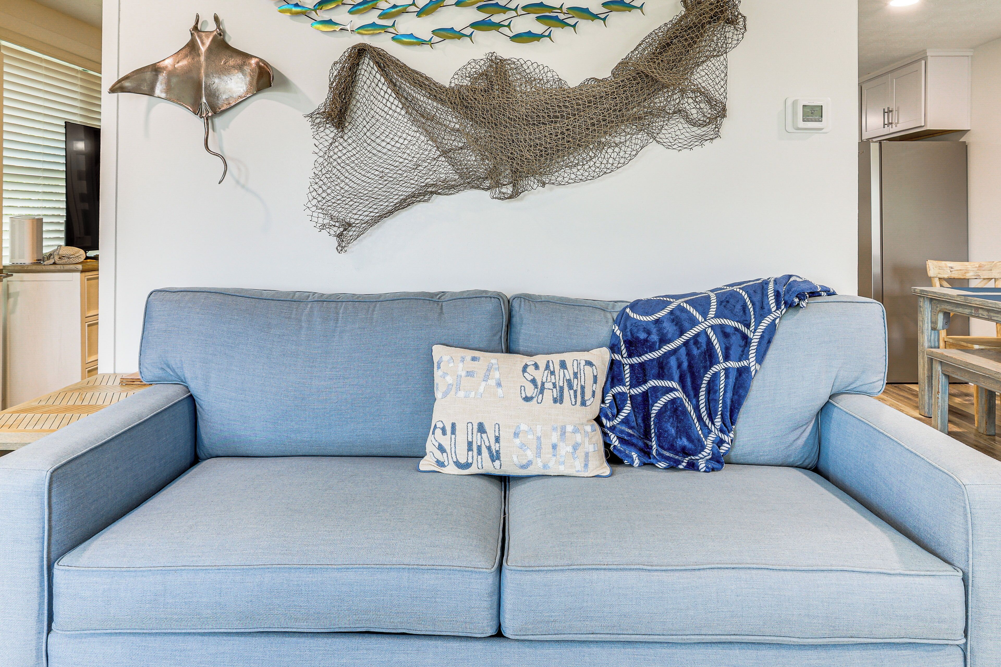 Ein hellblaues Sofa mit einem Kissen, auf dem "SEA SAND SUN SURF" steht, und ein dekoratives Netz an der Wand.