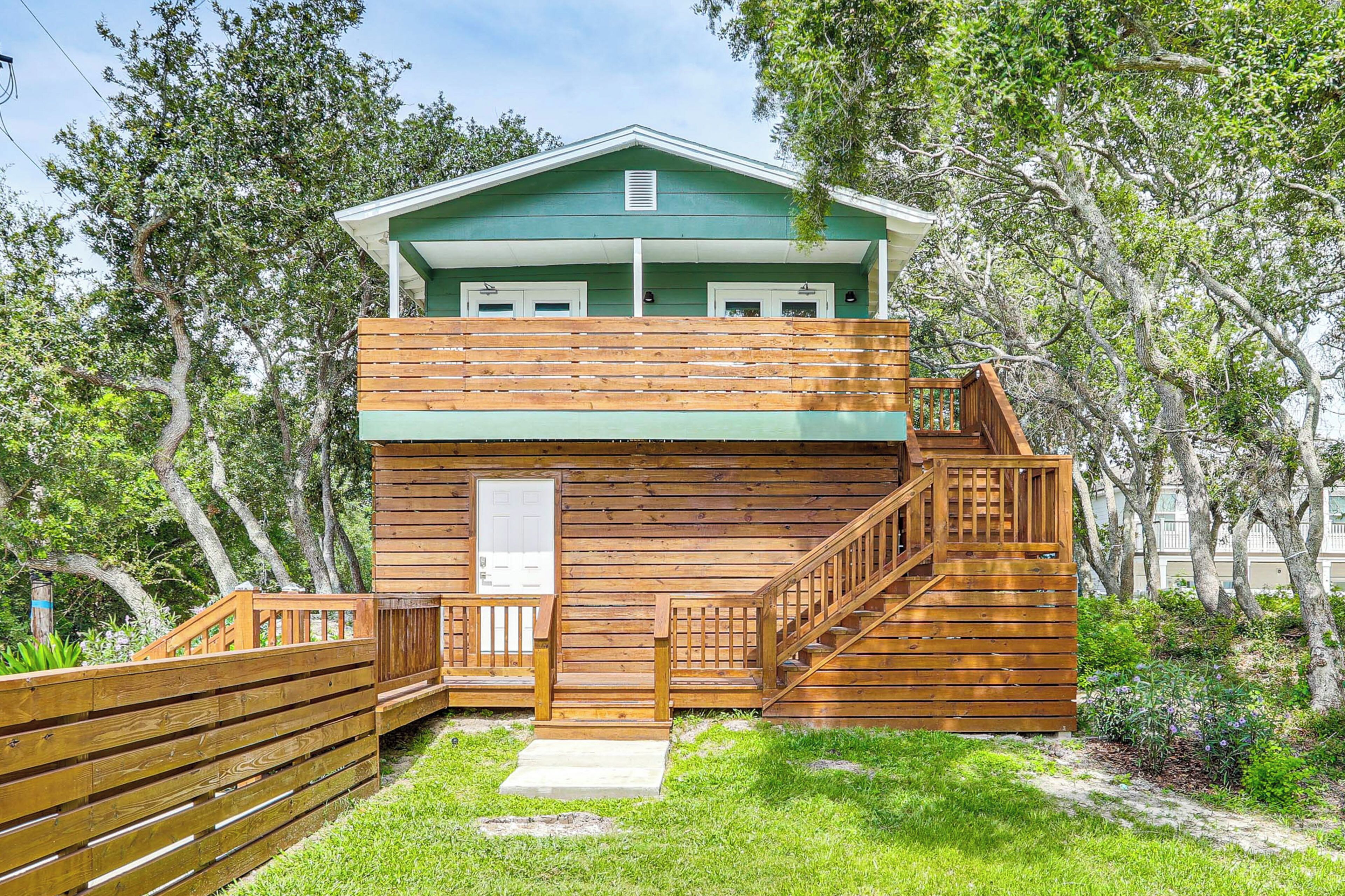 A two-story wooden cabin with a green roof, a wooden deck, and a staircase leading to the upper level.
