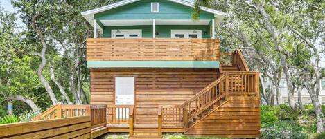 A two-story wooden cabin with a green roof, a wooden deck, and a staircase leading to the upper level.