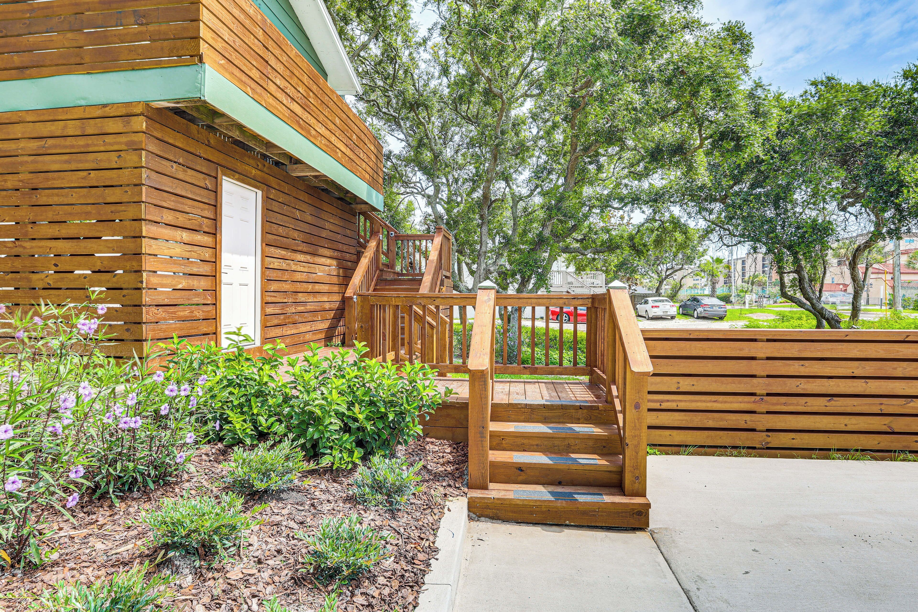 A wooden building with a wooden staircase leading to a deck, surrounded by greenery and trees.