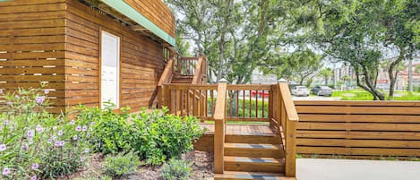 A wooden building with a wooden staircase leading to a deck, surrounded by greenery and trees.