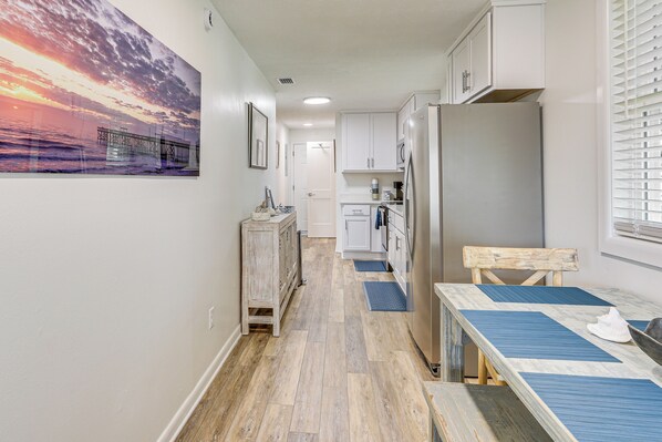 A narrow hallway with a wooden floor, a dining table with blue placemats, and a refrigerator.