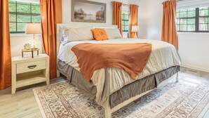 A bedroom with a bed, nightstand, lamp, and a large window with curtains. - 5 Mi to Dtwn Hiawassee: Creek-front Home w/ Deck (Hiawassee)