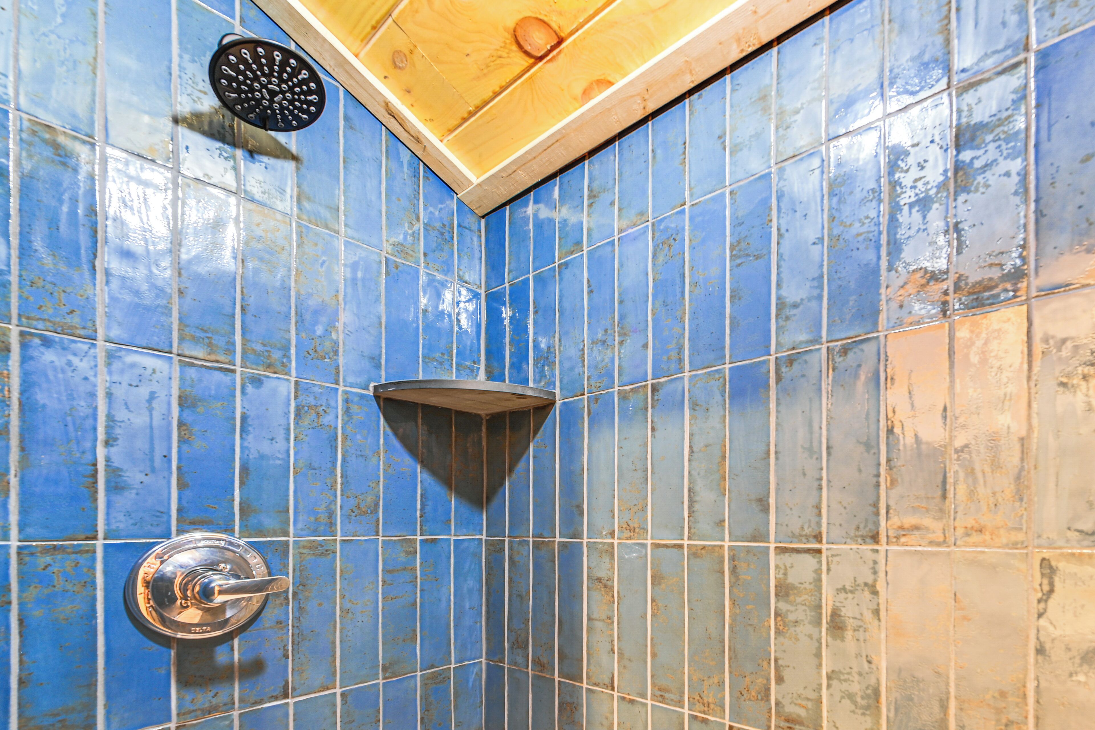 A shower with blue tiles and a wooden ceiling.