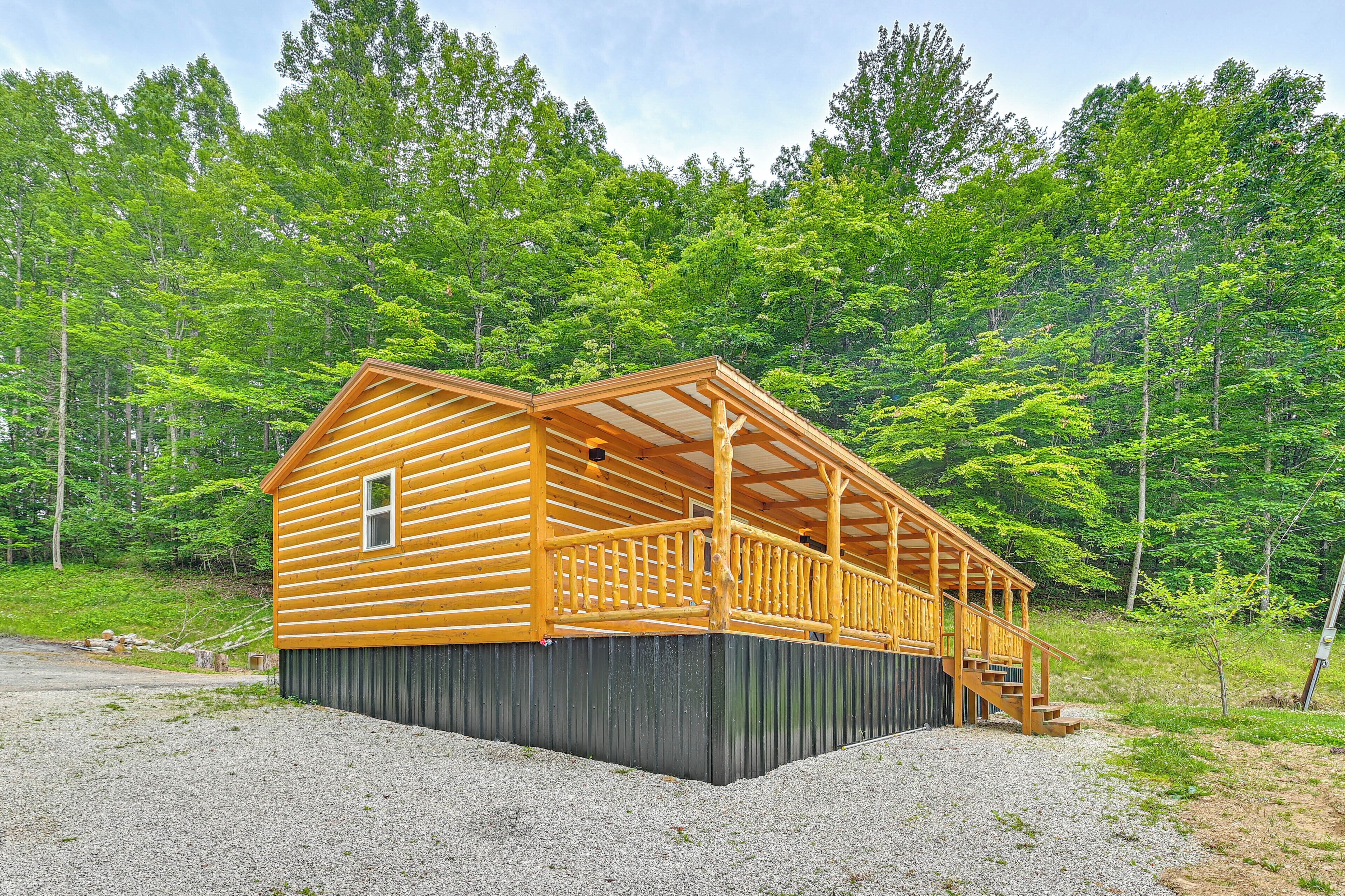 A log cabin with a porch and a small window, surrounded by a forest.