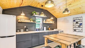 Eine Küche mit dunklen Schränken, einem Holztisch und hängenden Pendelleuchten.
