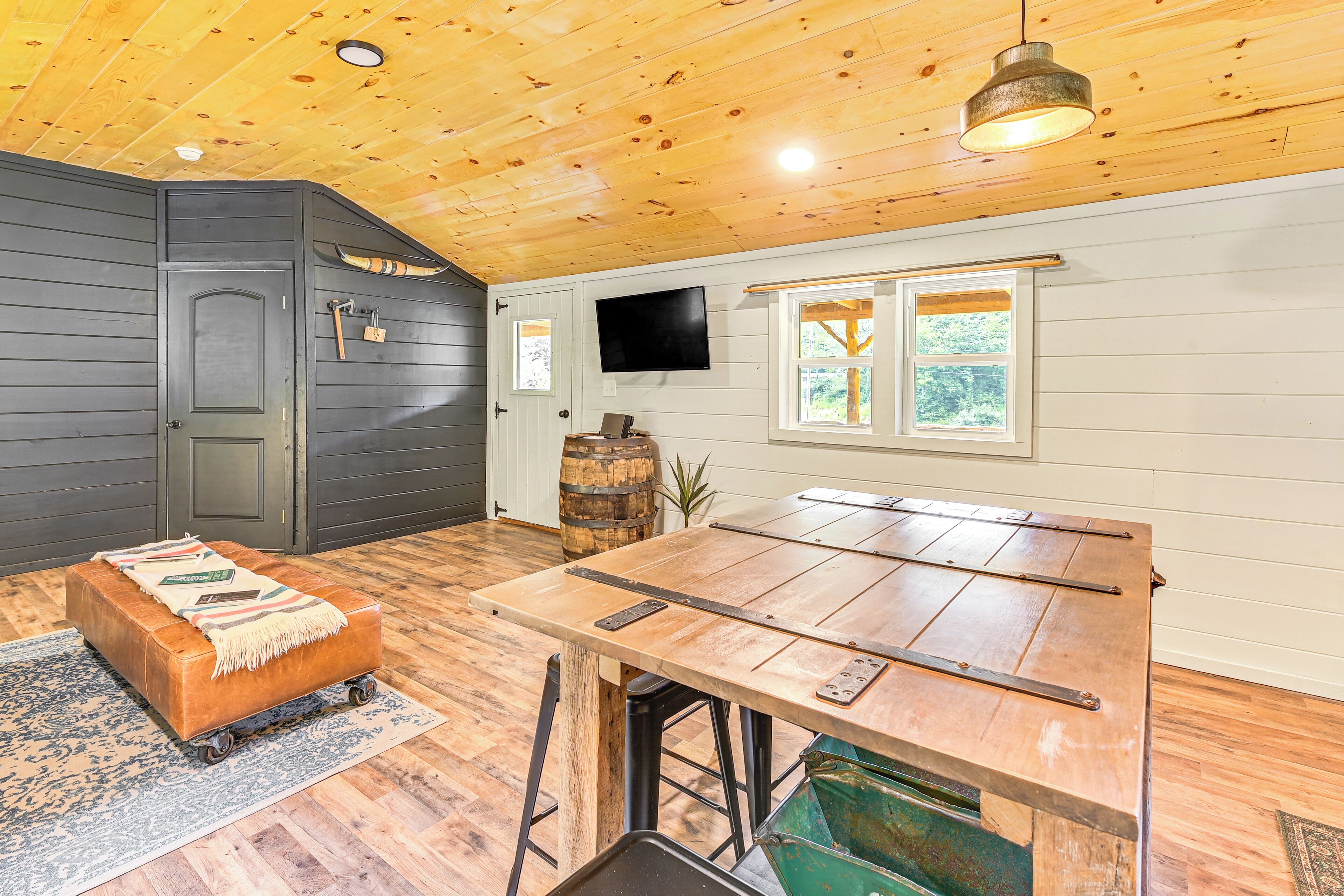 A rustic cabin interior with a wooden dining table, a bench, and a television mounted on the wall.