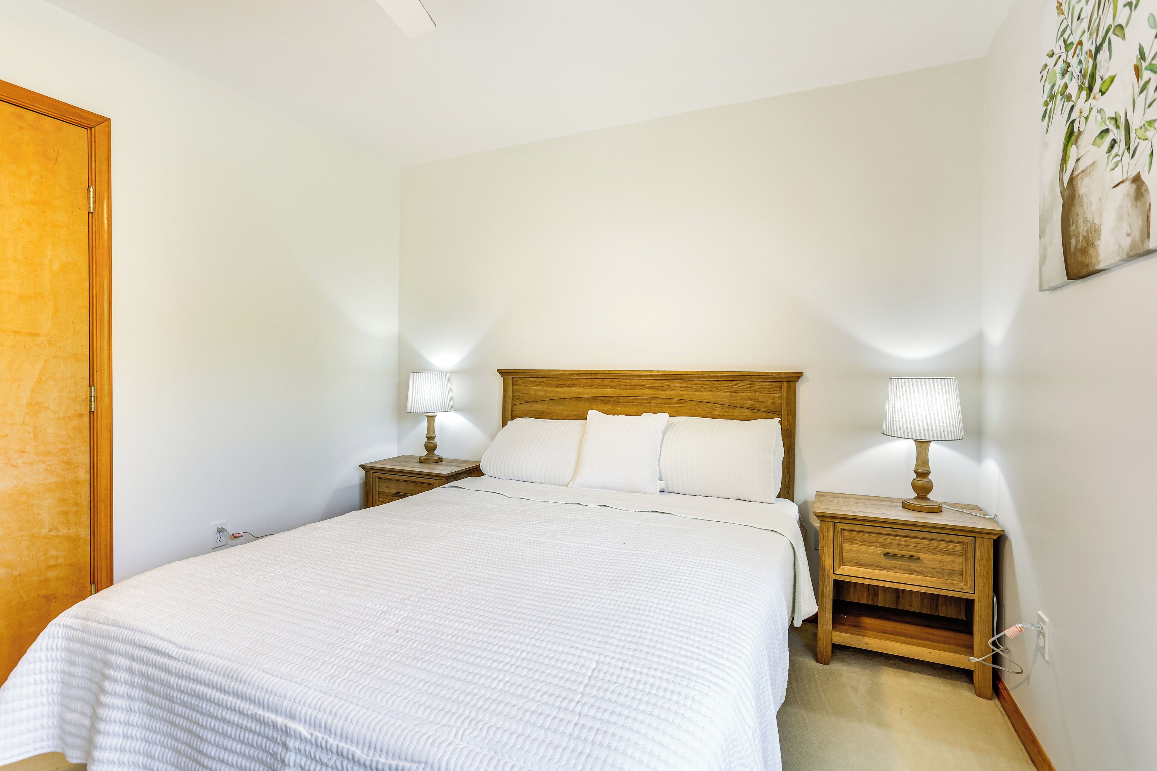 Un dormitorio con una cama grande, dos mesitas de noche con lámparas, un cabecero de madera y un cuadro colgado en la pared.