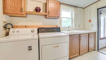 A laundry area with a washer and dryer, wooden cabinets, a window with lace curtains, and a sink.