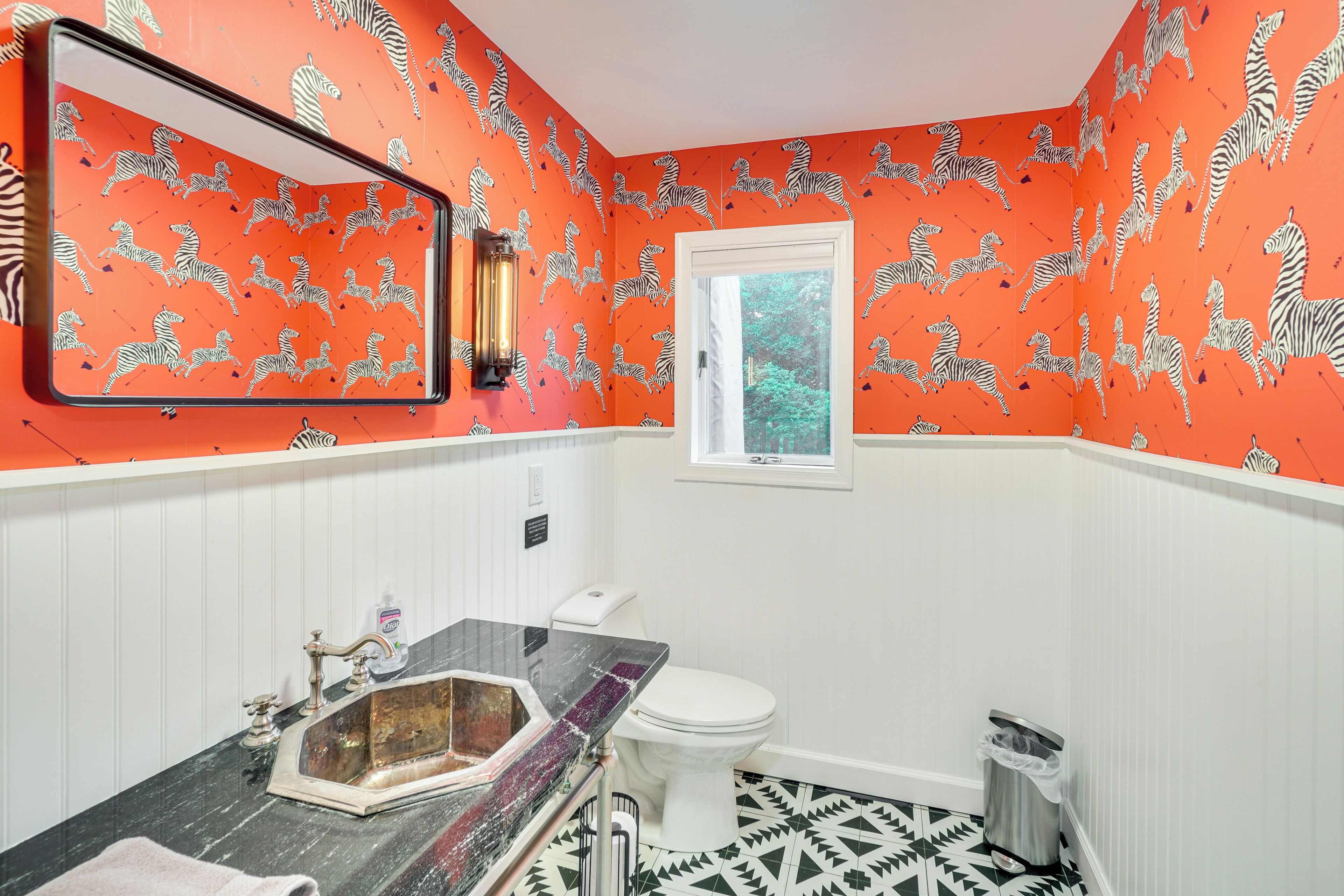 Un bagno con carta da parati a motivi zebrati, pavimento a scacchi bianchi e neri, un lavabo in marmo e una finestra vista verde.