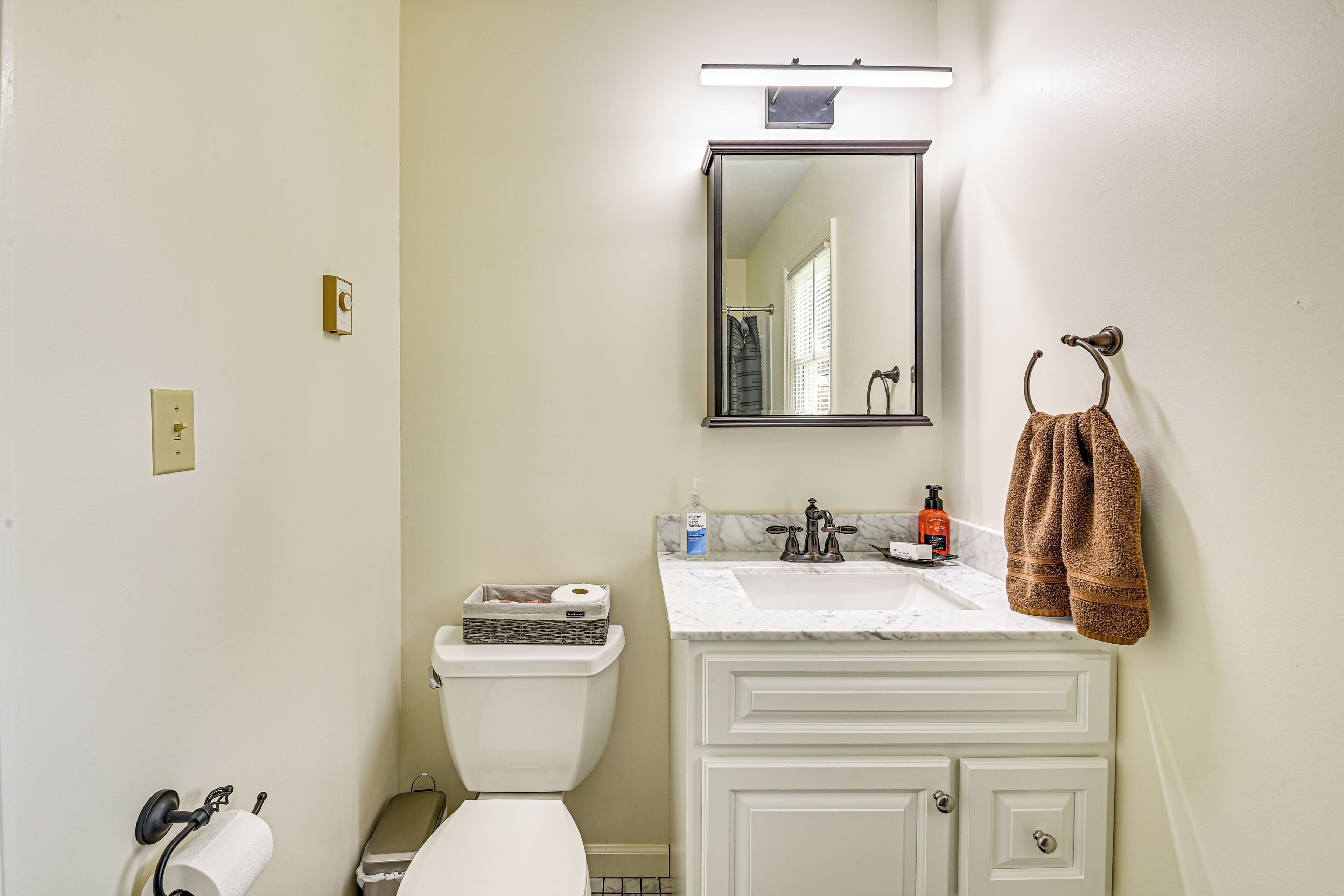 A bathroom with a toilet, sink, mirror, towel rack, and a toilet paper holder.