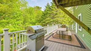 Una terraza con parrilla, mesa de picnic y sillas, rodeada de exuberante vegetación.