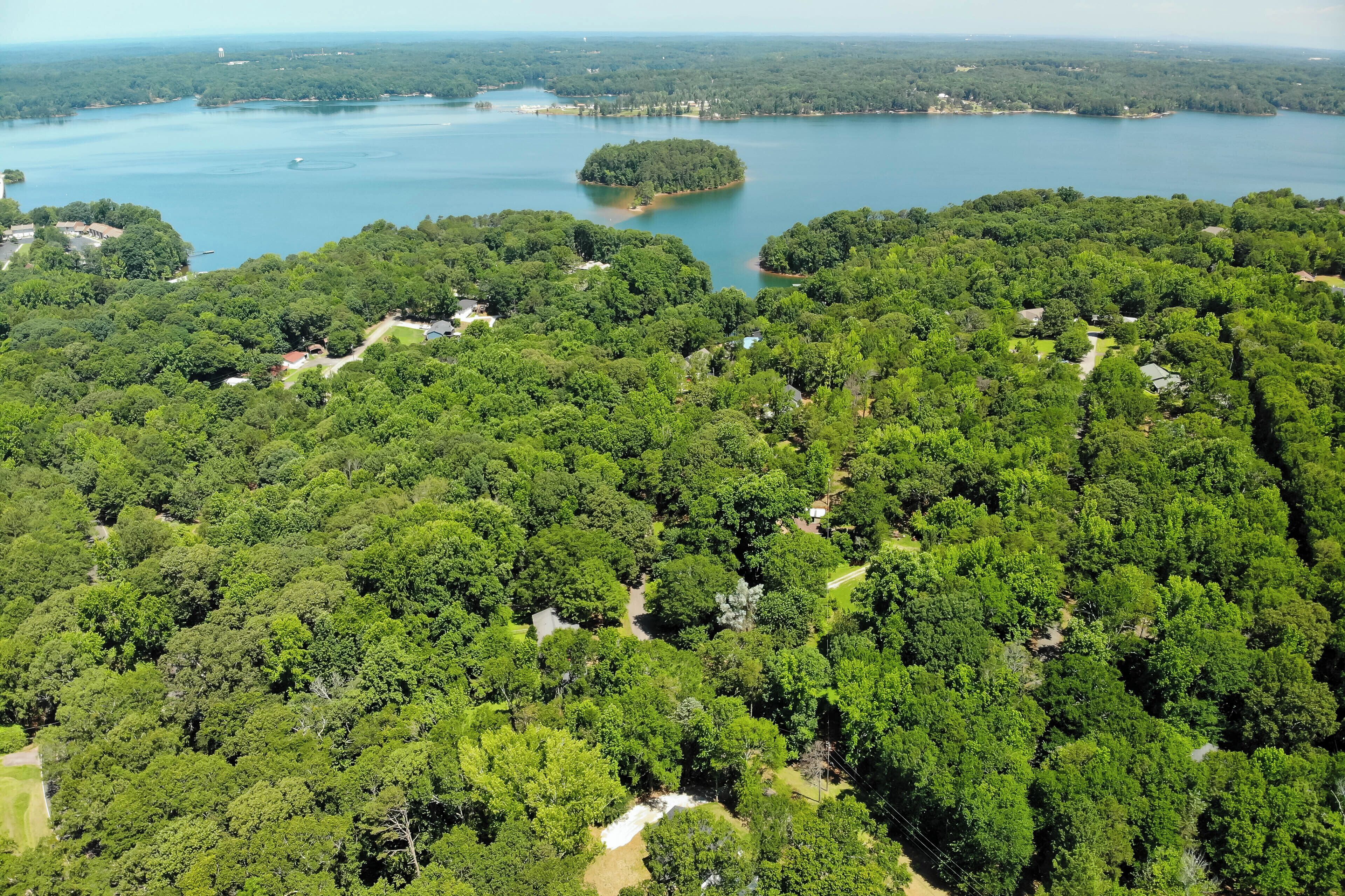 Une vue aérienne d’une zone boisée avec un lac, une petite île et quelques bâtiments dispersés.
