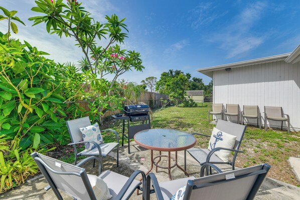 Un jardin avec un barbecue, un espace extérieur aménagé avec des chaises et une table, et une végétation luxuriante.