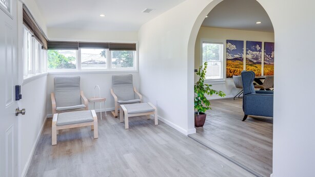 Una habitación amplia con dos sillas de madera, una mesita y un ventanal grande.