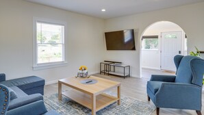 Una sala de estar con sofá, una mesa de centro, televisor montado en la pared y una puerta que da a otra habitación.