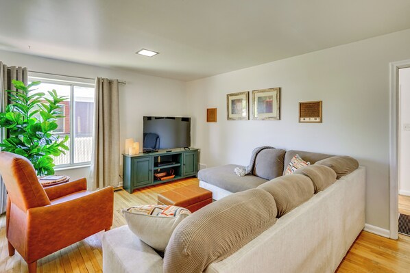 A living room with a sofa, armchair, TV, and a potted plant. - Private Patio & Gym: Spacious Salt Lake City Home! (Salt Lake City)