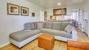 A living room with a sectional sofa, a small ottoman, and a dining area with a table and chairs.