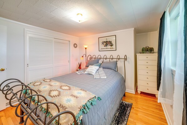 A bedroom with a bed, a dresser, a lamp, and a window with curtains.