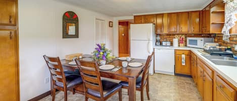 A dining area with a wooden table and chairs, a refrigerator, a microwave, and a sink.